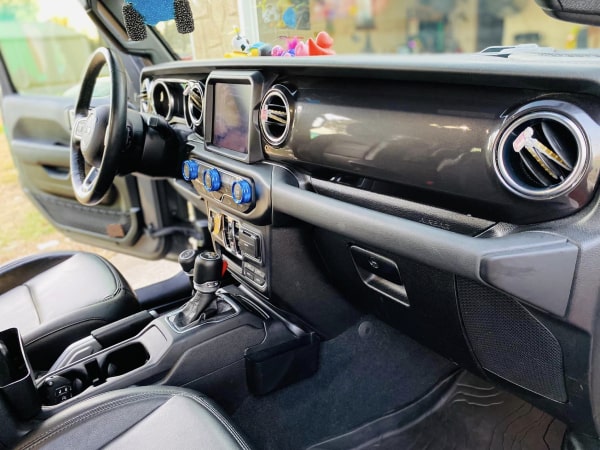 Dashboard view of a Jeep displaying the steering wheel, gauges, and infotainment system with colorful figurines on the dash.
