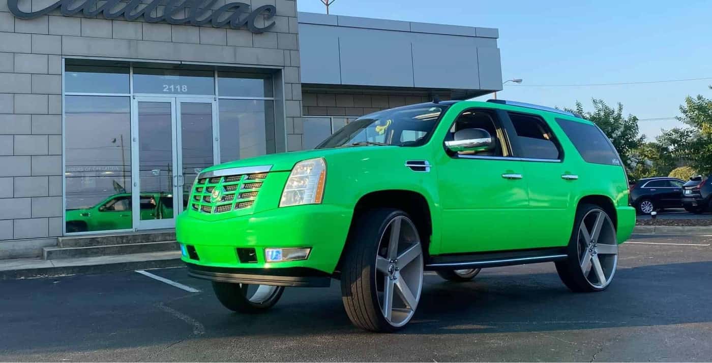 A vibrant green SUV with chrome rims parked in front of a modern building with large glass windows and the building number 2118 visible.