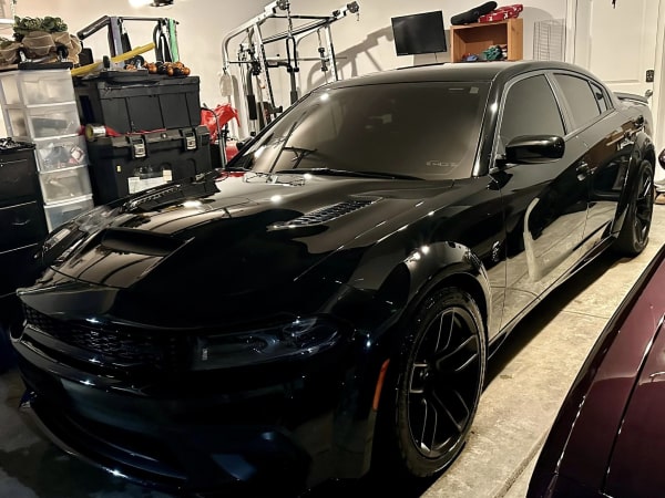 Glossy plum-colored Dodge Challenger with black rims parked in a driveway next to a brick house with a garage in the background.