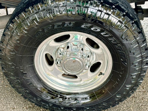 Three Ford Mustangs parked in a row on a shaded street, with the reflection of trees on the car surfaces.