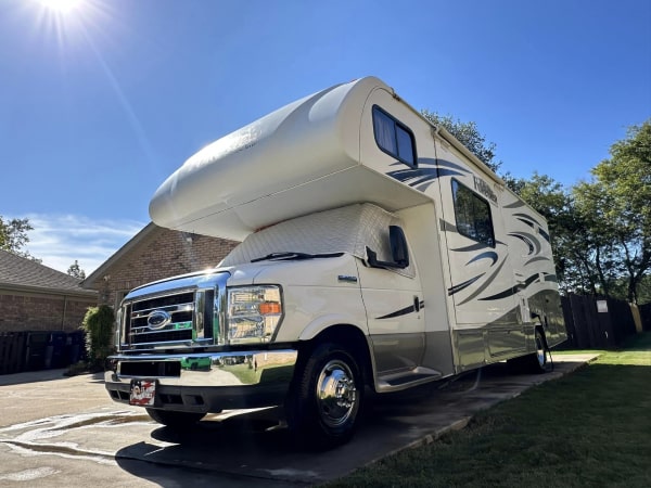 A beige Forester RV parked in a driveway, with a well-maintained lawn and a residential building in the background.